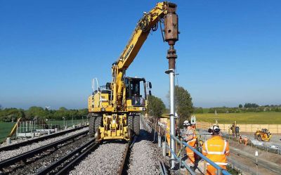 Railway track maintenance work with a Komatsu road-rail excavator installing helical piles alongside the track